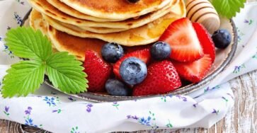 Fluffy pancakes stacked with syrup, butter, and fresh fruits
